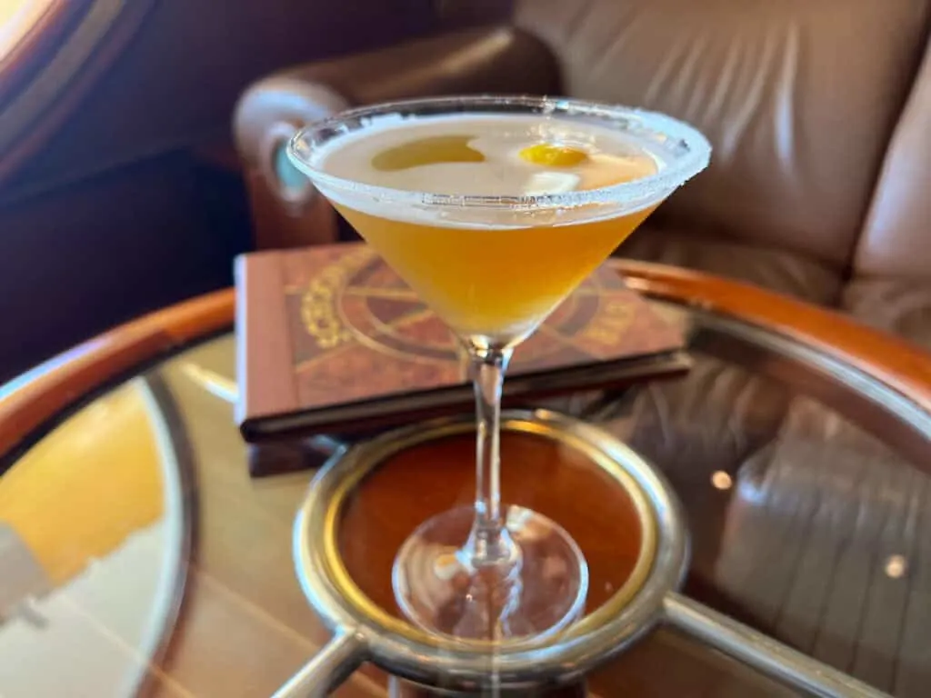 amber colored liquid with lemon slice in martini shaped glass (upside down triangle shaped glass) sitting on top of round glass table