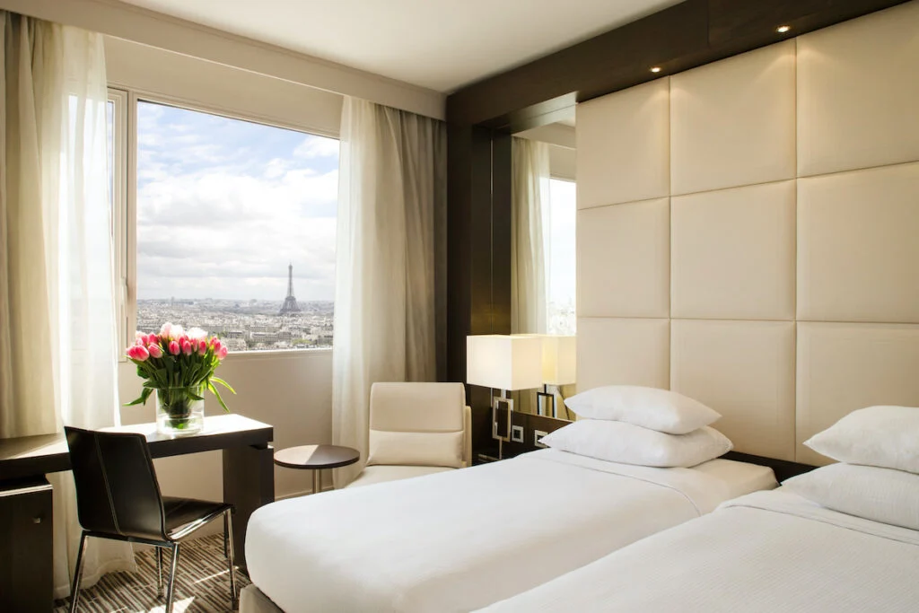 modern hotel room with light beige colors overlooking a tall triangle tower; Hyatt Regency Paris Etoile hotel room with view of the Eiffel Tower